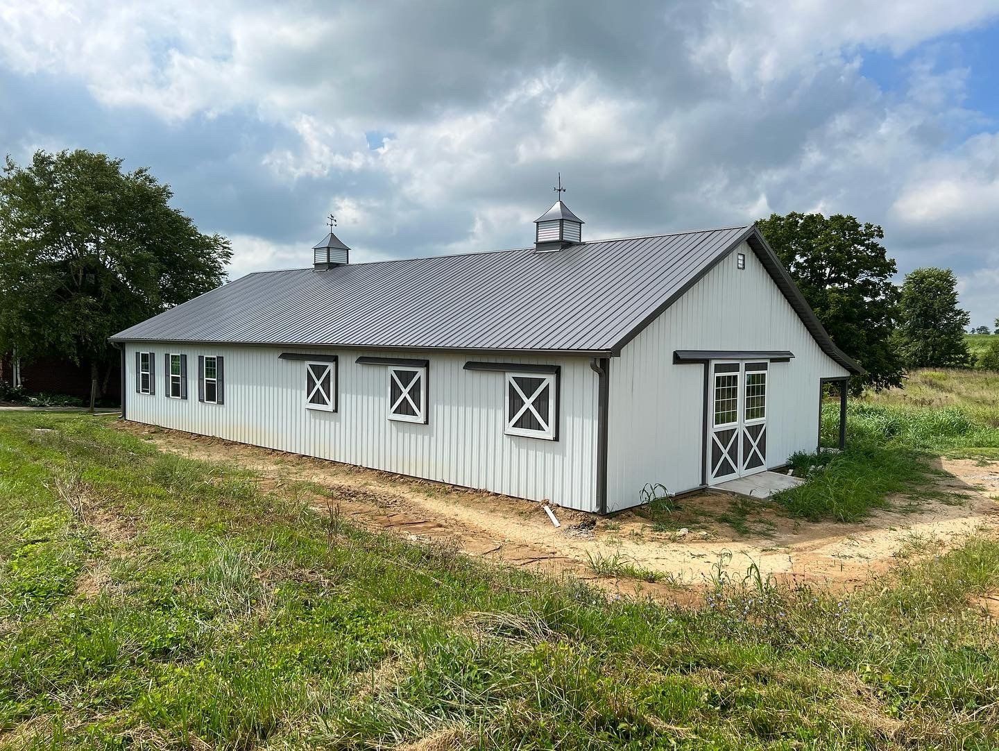 White barn with a gray roof and dark brown trim, set in a grassy field under a cloudy sky.
