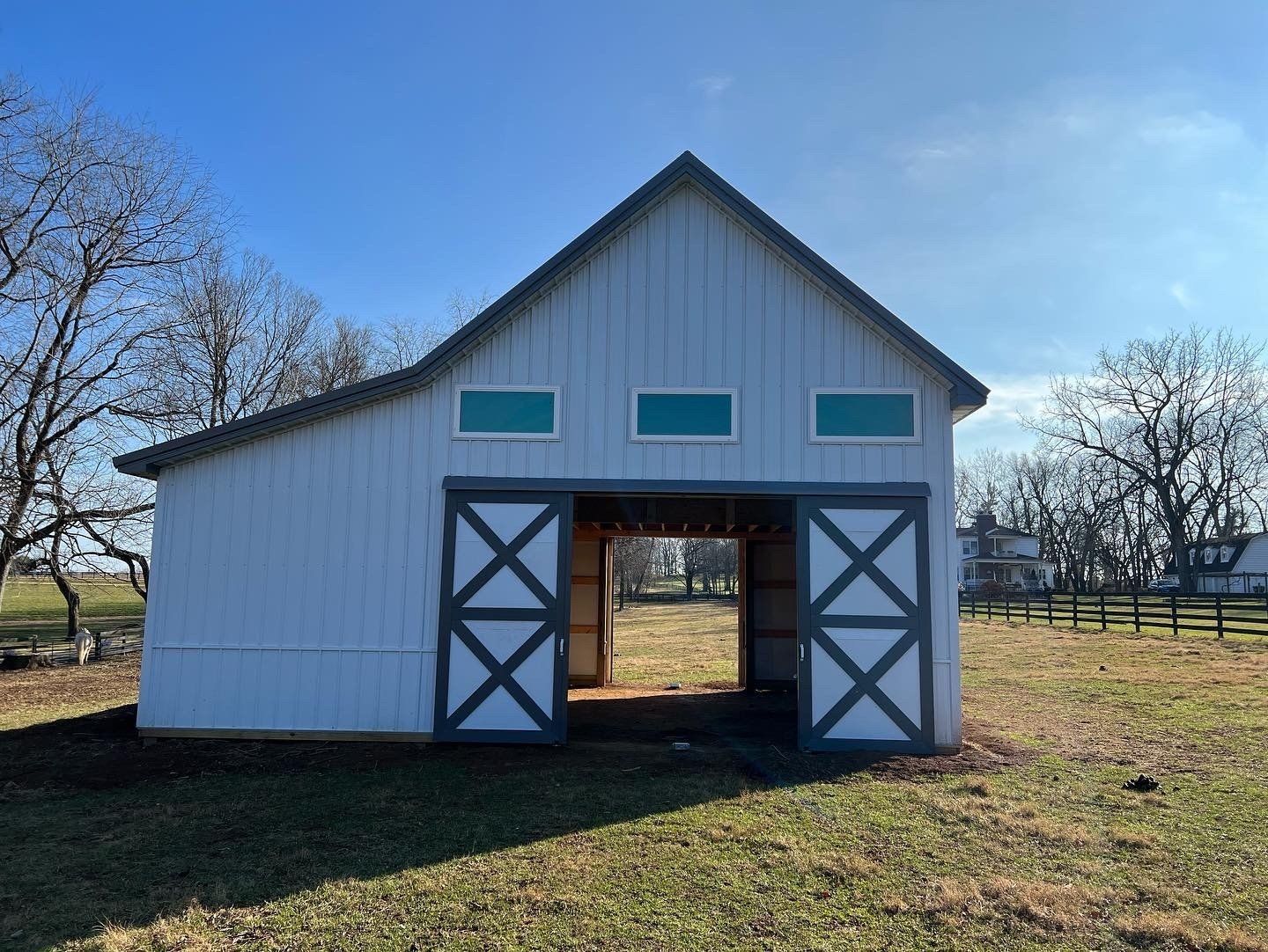 White barn with teal accents and large sliding doors, in a grassy field on a sunny day.