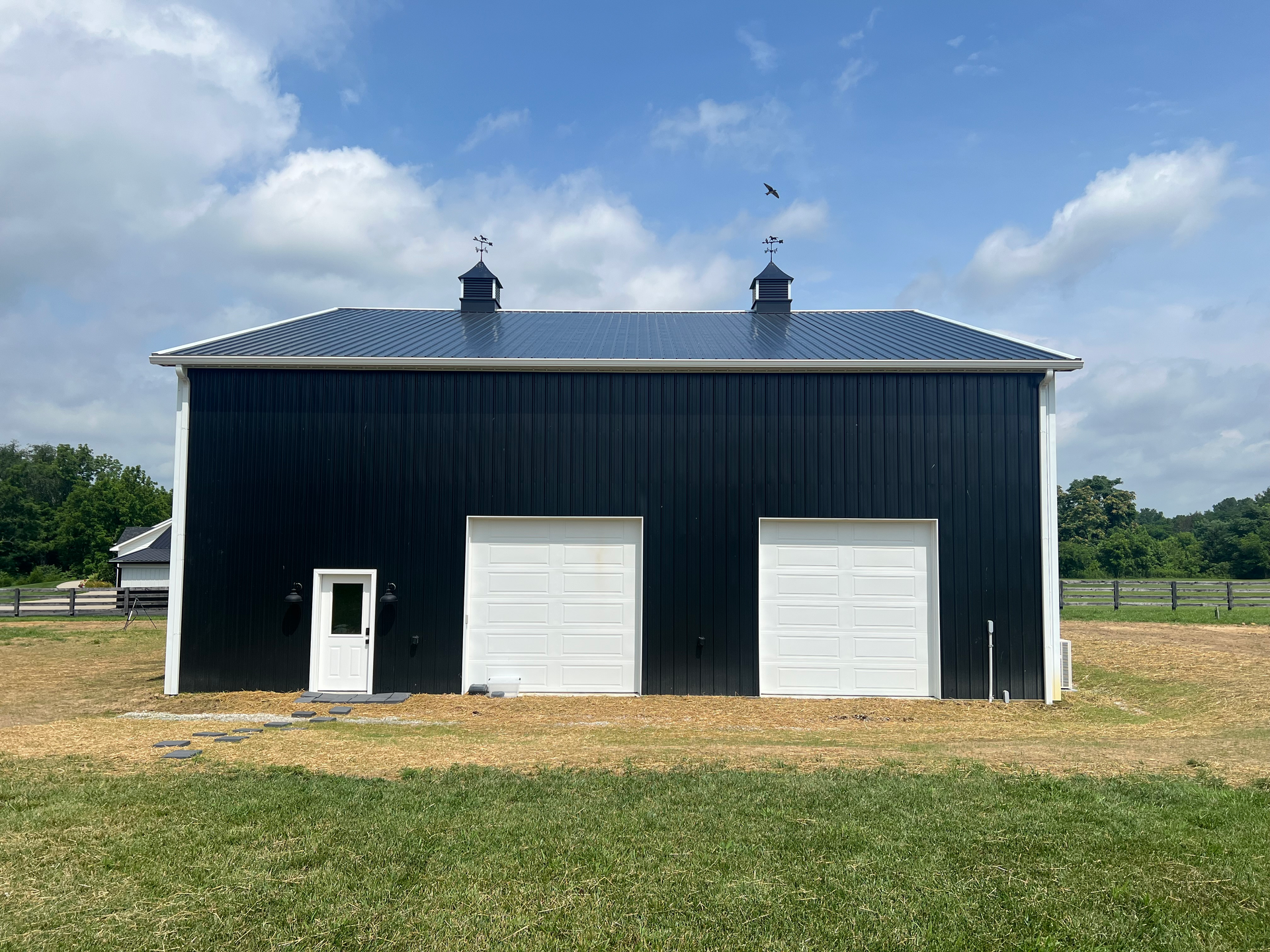 Black and white two-story barn under a blue sky. The building has two garage doors and a white door.