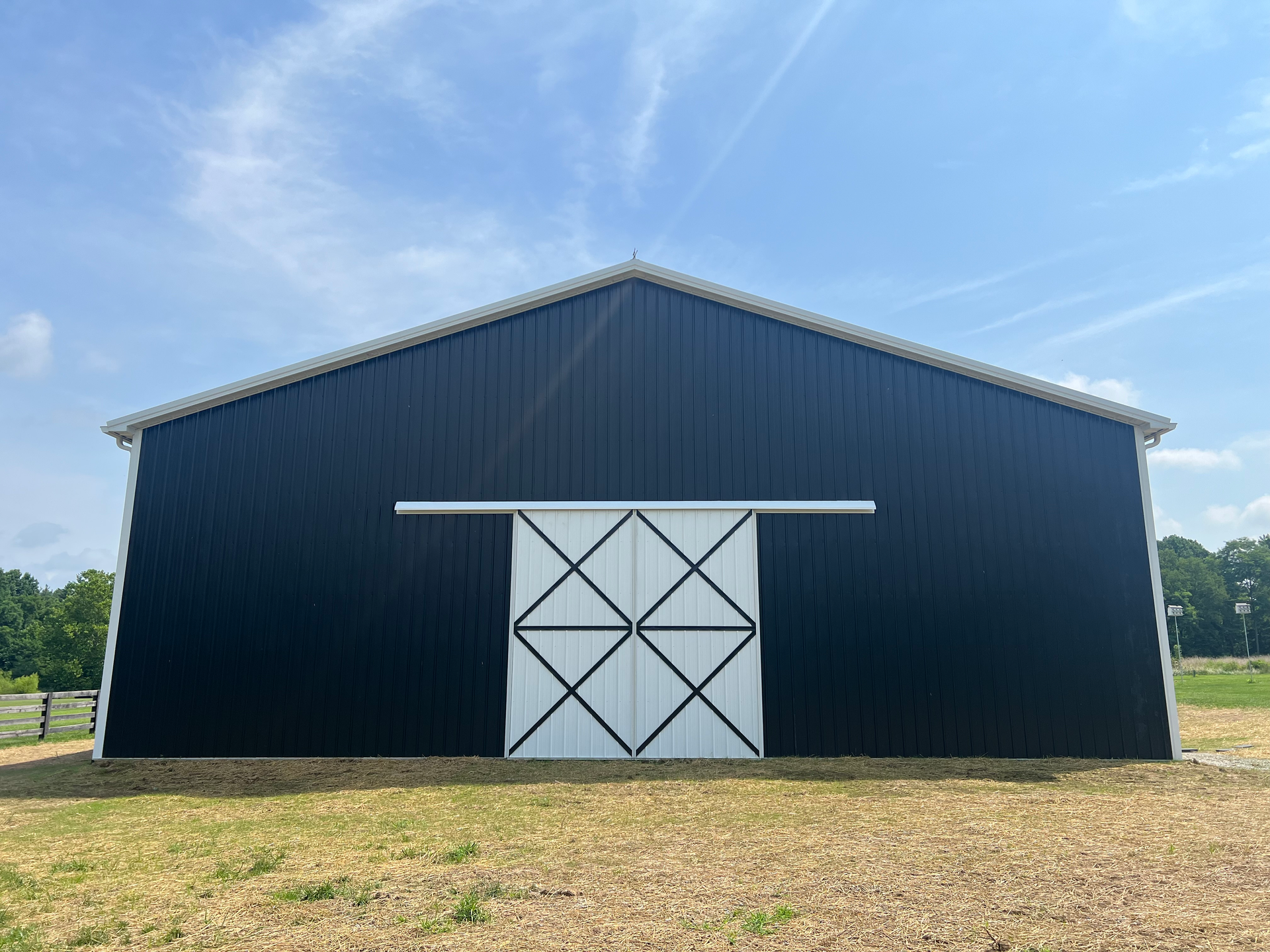 A dark blue barn with a large white sliding door is set against a blue sky.