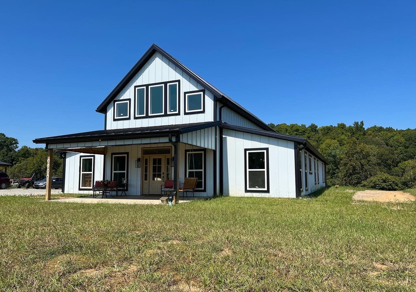 Two-story white house with black trim and a porch, set against a clear blue sky and grassy field.