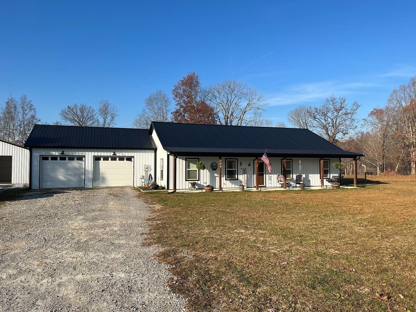 White ranch home with a black roof and two-car garage, set on a gravel driveway and grassy lawn under a blue sky.