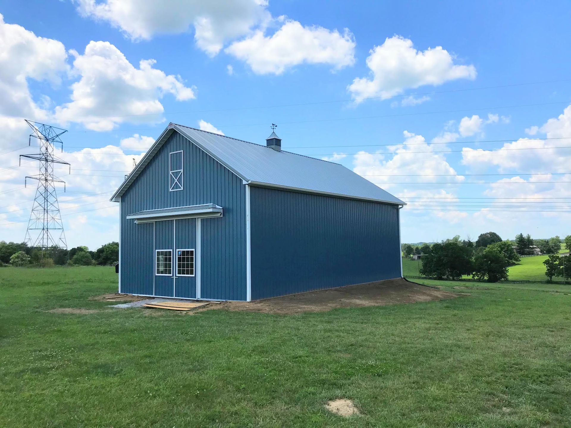 Blue barn with a metal roof on a grassy field under a blue sky with fluffy clouds.