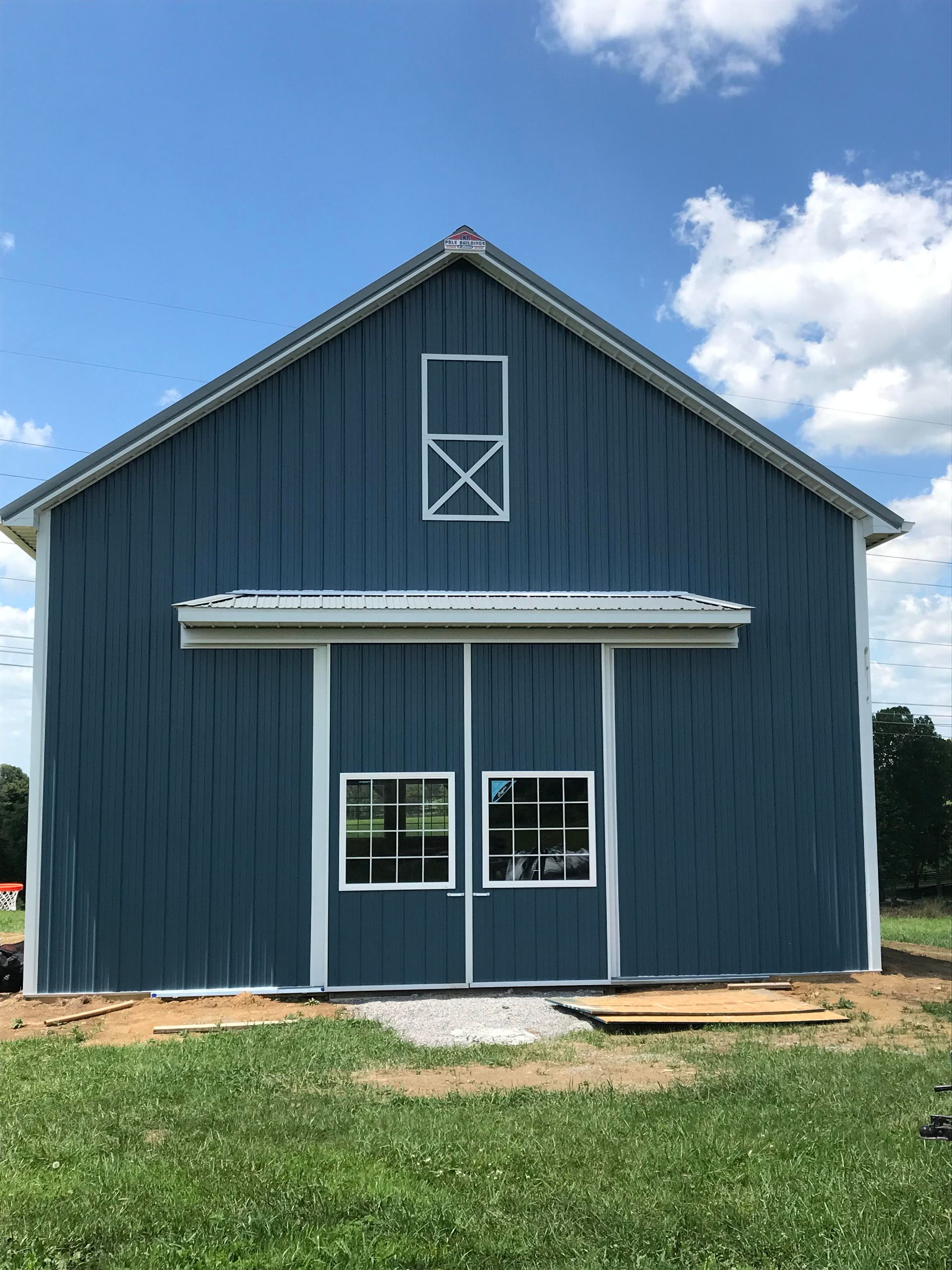 Blue barn with white trim and a gray gravel path, set against a bright blue sky.