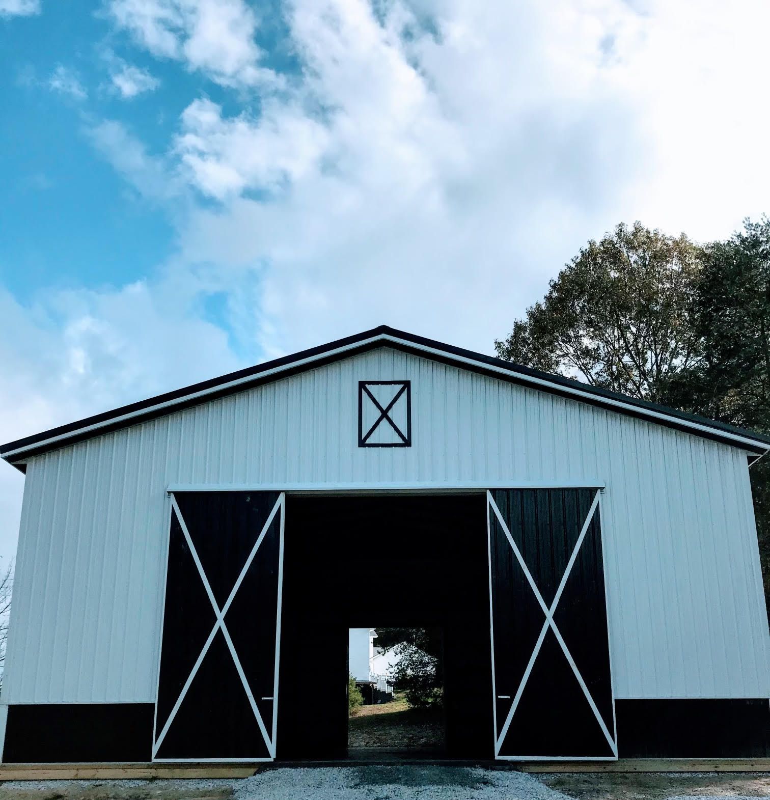 White barn with black doors open, under a cloudy blue sky. A tree is visible through the open doors.