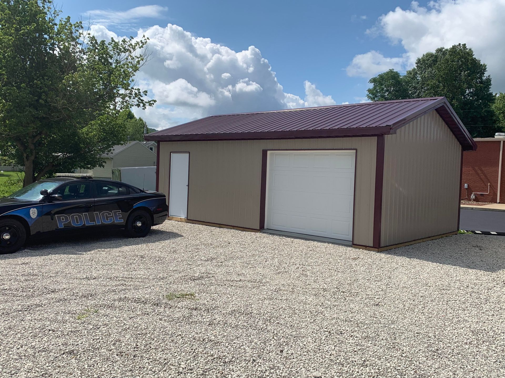 A tan metal building with a maroon roof and trim. A police car is parked in front.
