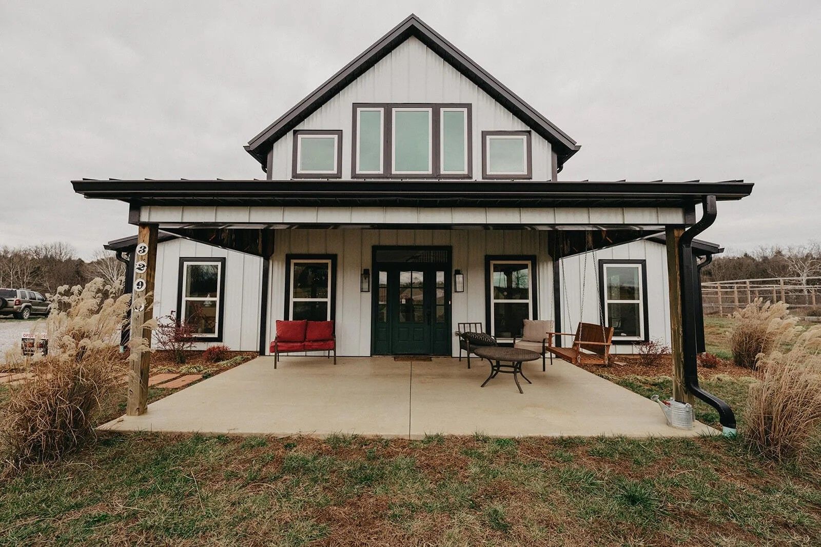 White farmhouse with a black roof and porch, dark green door, and patio furniture.