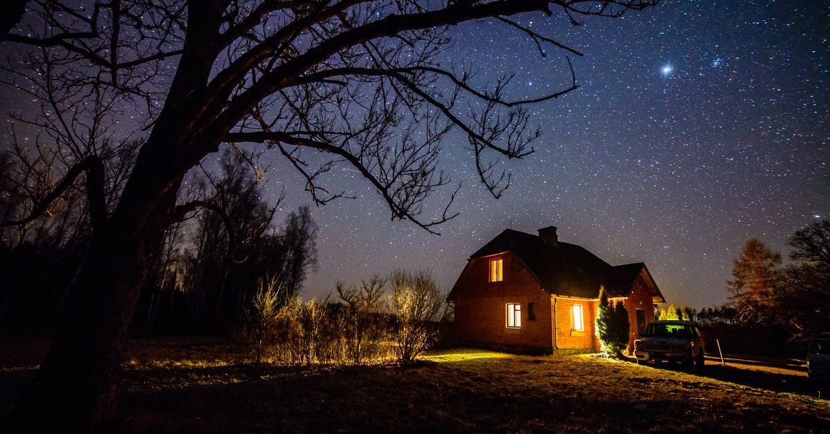 Stars shine brightly over a barn house with a car parked in front of it at night.