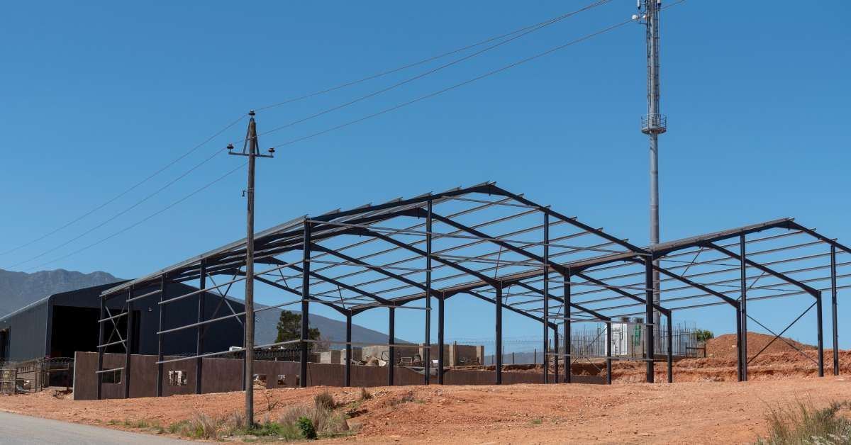 The foundation of two pole barns being constructed on a farm with a cellphone tower and mountains in the background.