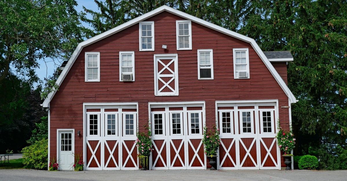 A two-story red barn with white trim, several windows, and three large entrances beside a small door.
