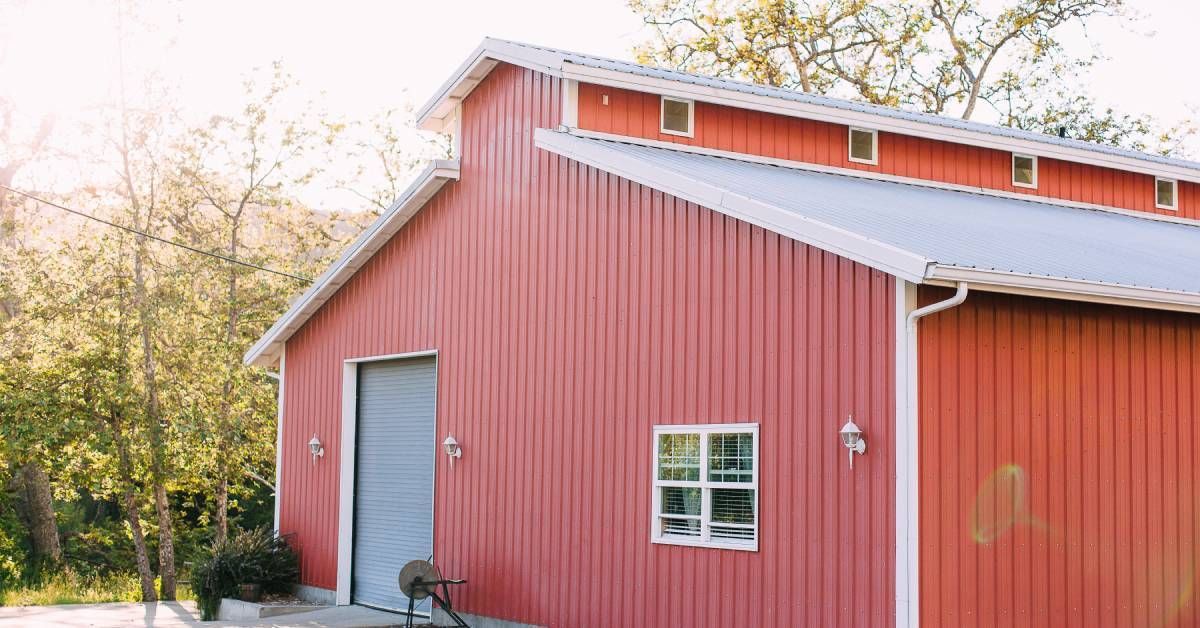 The exterior of a large red barn with a vaulted roof. The side of the barn has a gray roller door an