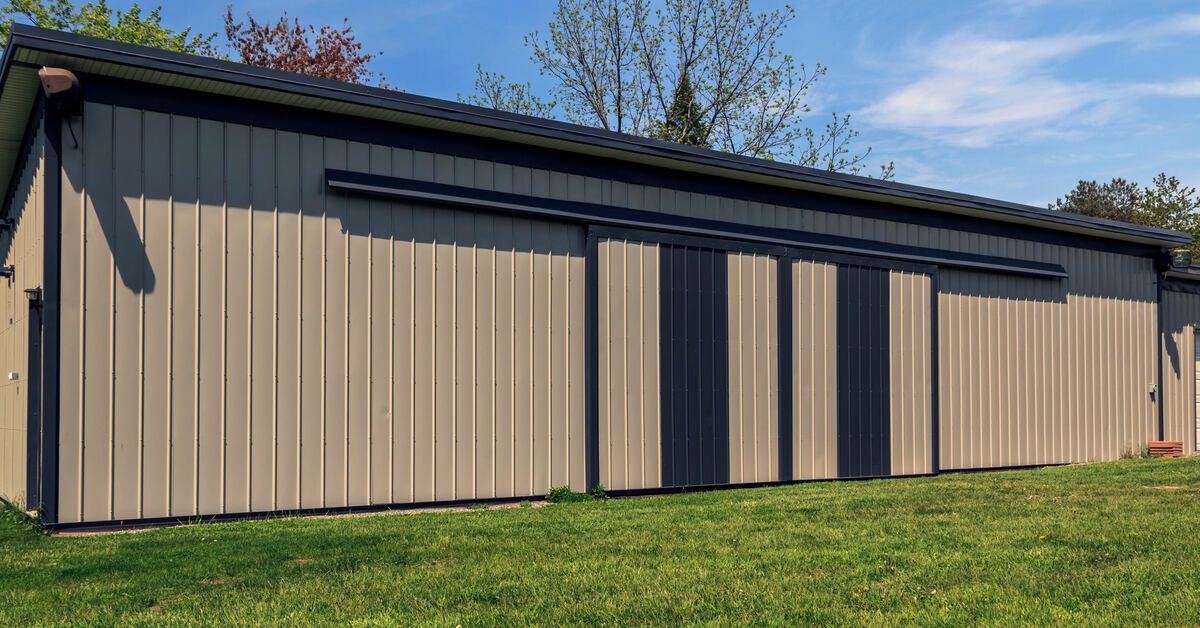 The exterior of a brown metal barn on a sunny day. The barn has a white garage door on one side of t