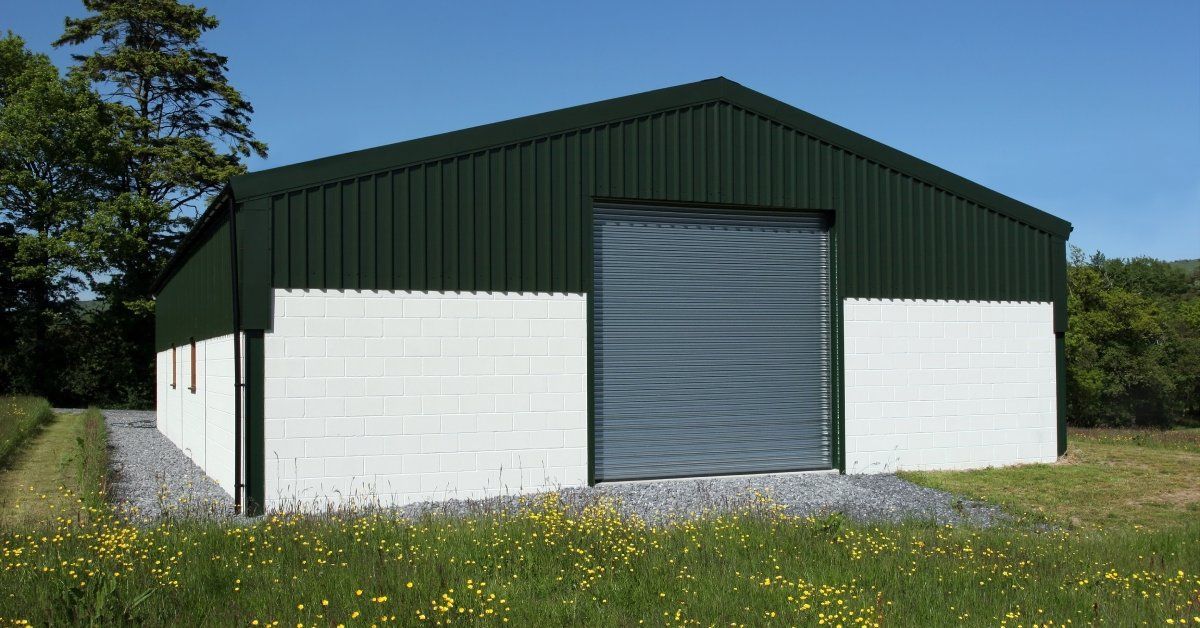 The exterior of a barn with green siding and white brick. The barn has a gray roll-up door in the front.