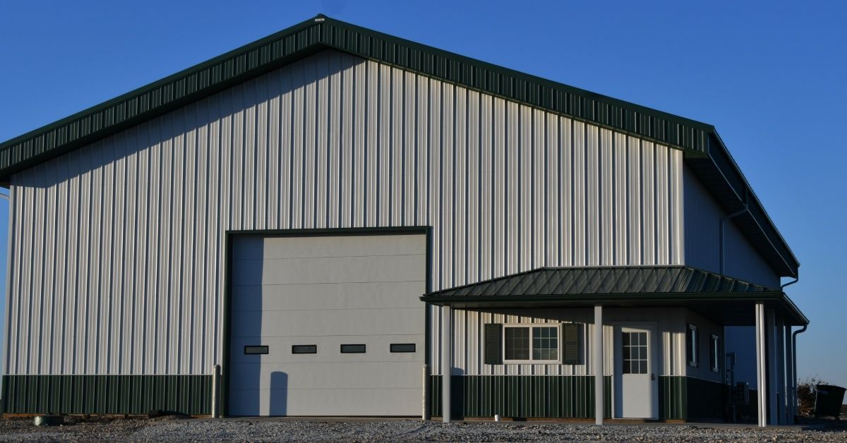 A large green and white metal barn on a sunny day. The front of the barn has an overhead door with small windows.