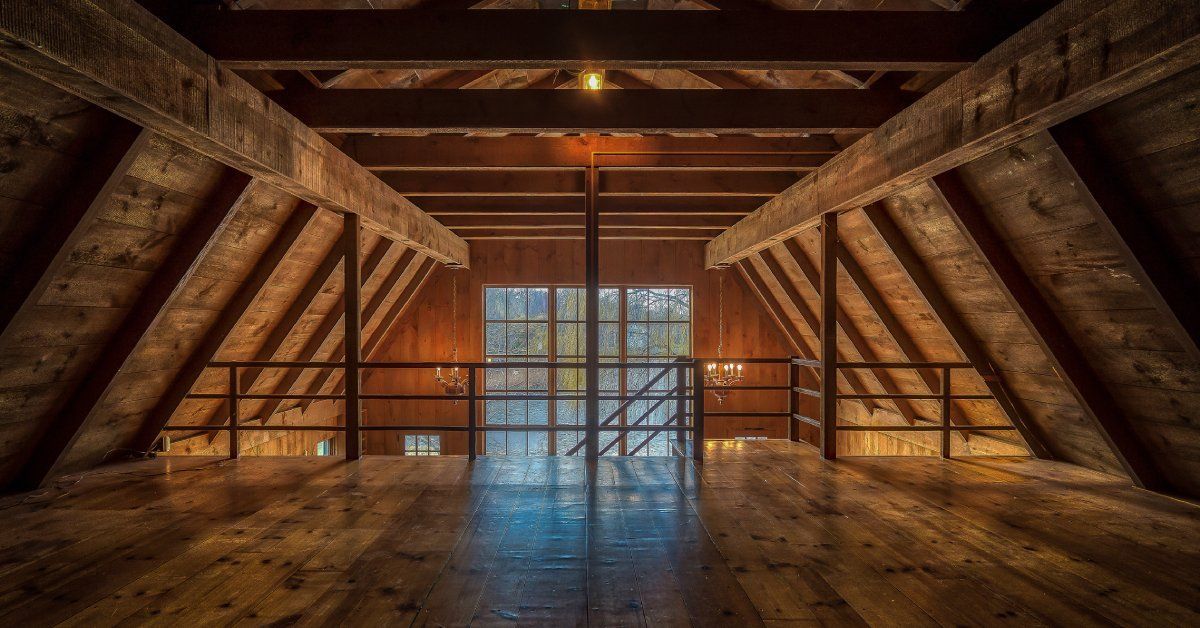 The interior of the second level of a modern barn. The barn has wood floors, two hanging chandeliers, and wood beams.