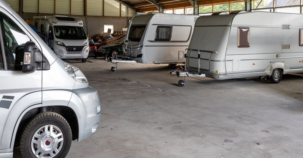 Several silver RVs and caravans parked inside a large structure with a concrete floor and a peaked r