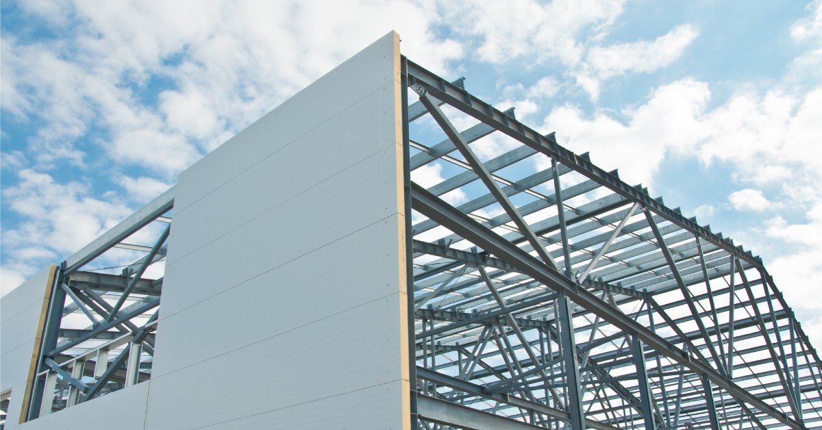 The metal frame of a large building under construction with insulation panels on one wall on a cloudy day.