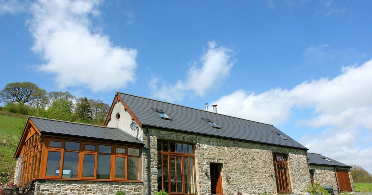 The exterior of a renovated barn with stone siding, wood trim, and a peaked roof with three skylights.