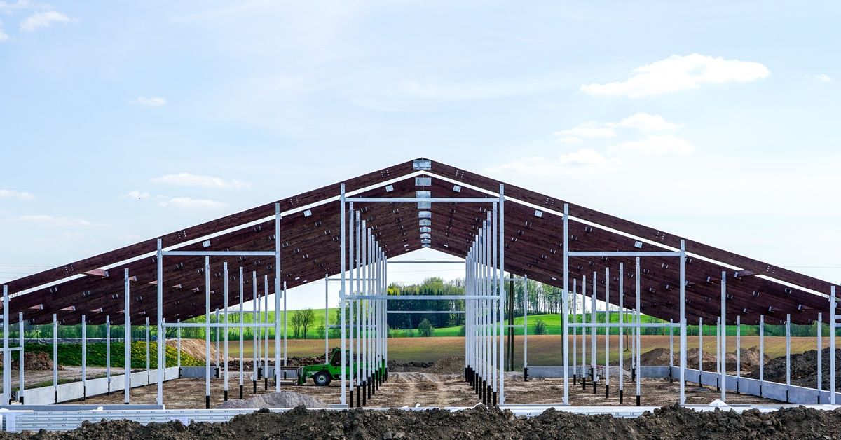 A metal building with a peaked roof under construction with piles of dirt surrounding the structure.