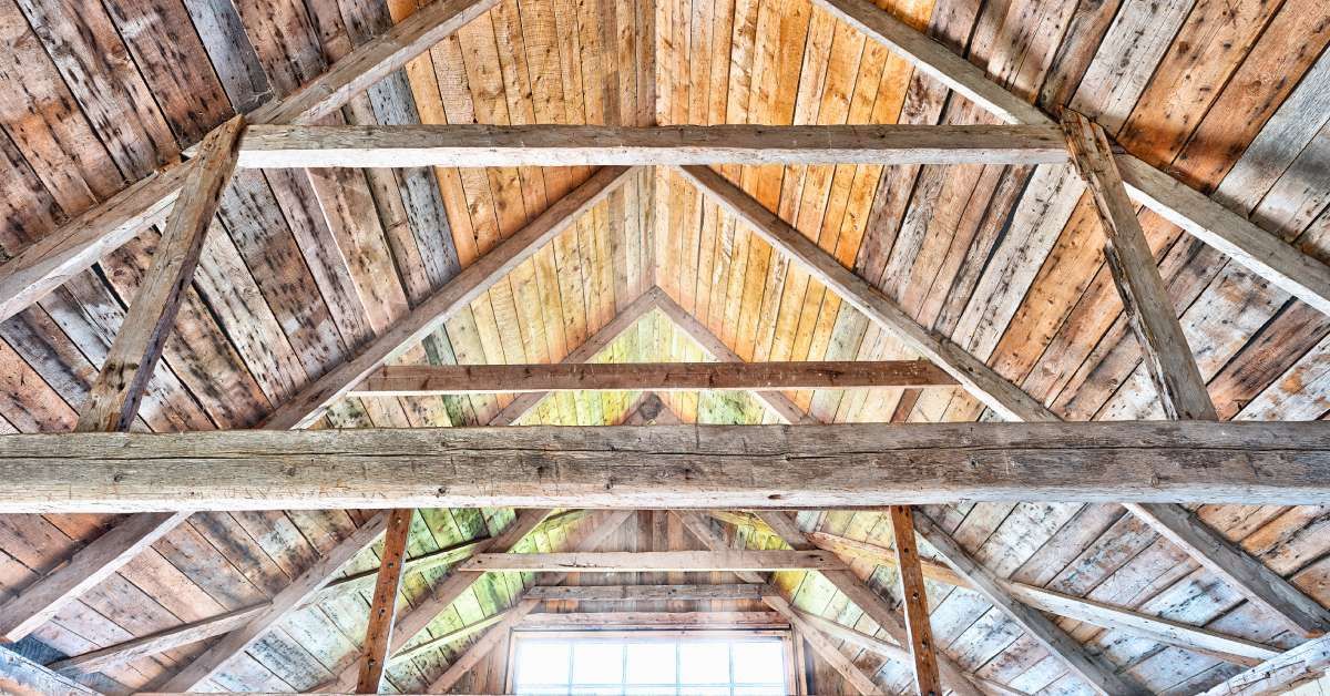 An upward-angle of a home's upper-level window with light shining in. The interior is made up of wooden beams.