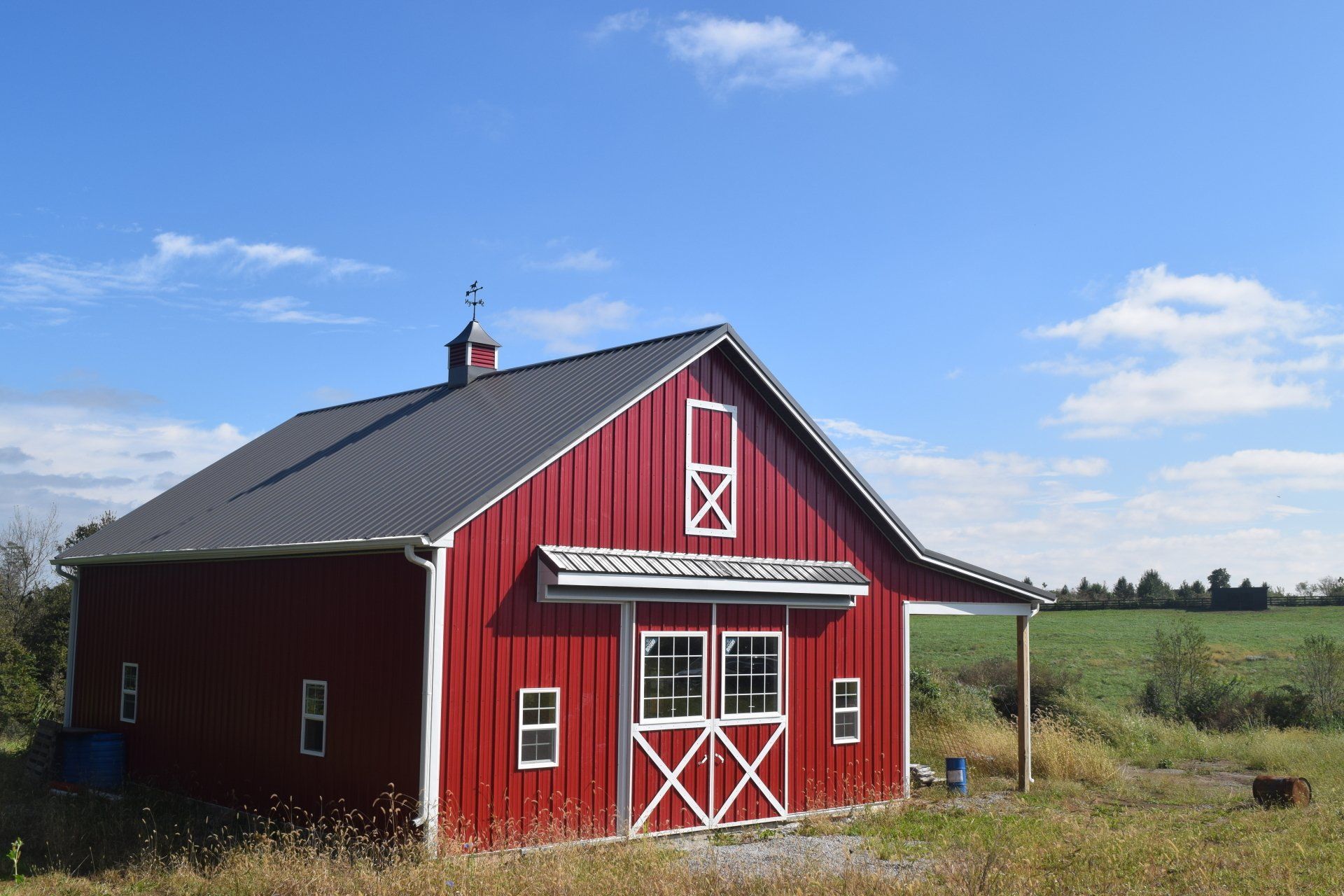 Red barn with white trim and a dark gray roof under a blue sky with wispy clouds.