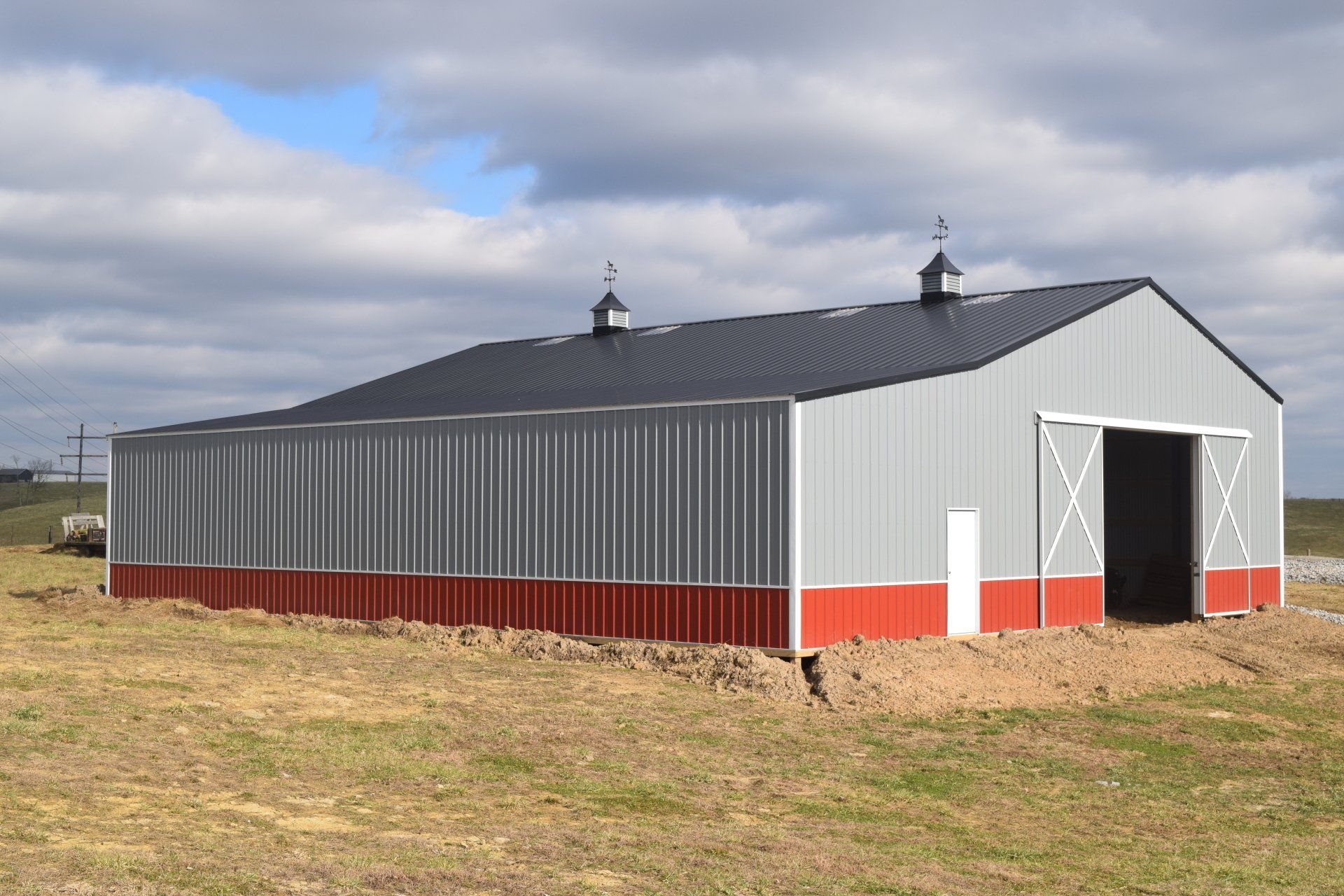 Large metal barn with a red base, gray walls, and black roof under a cloudy sky.
