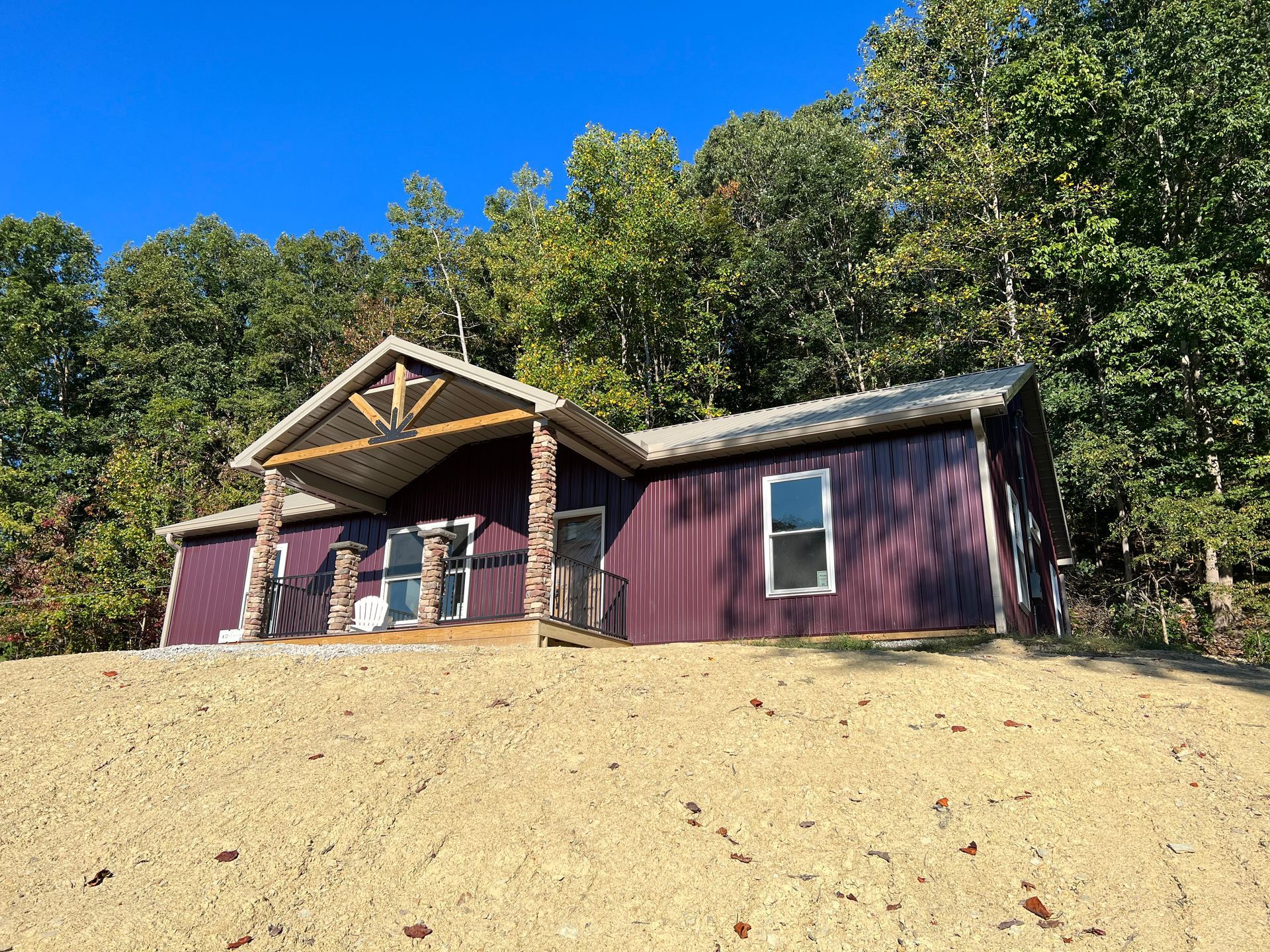 Purple cabin with stone columns and wooden accents, set against a hillside with trees under a blue sky.
