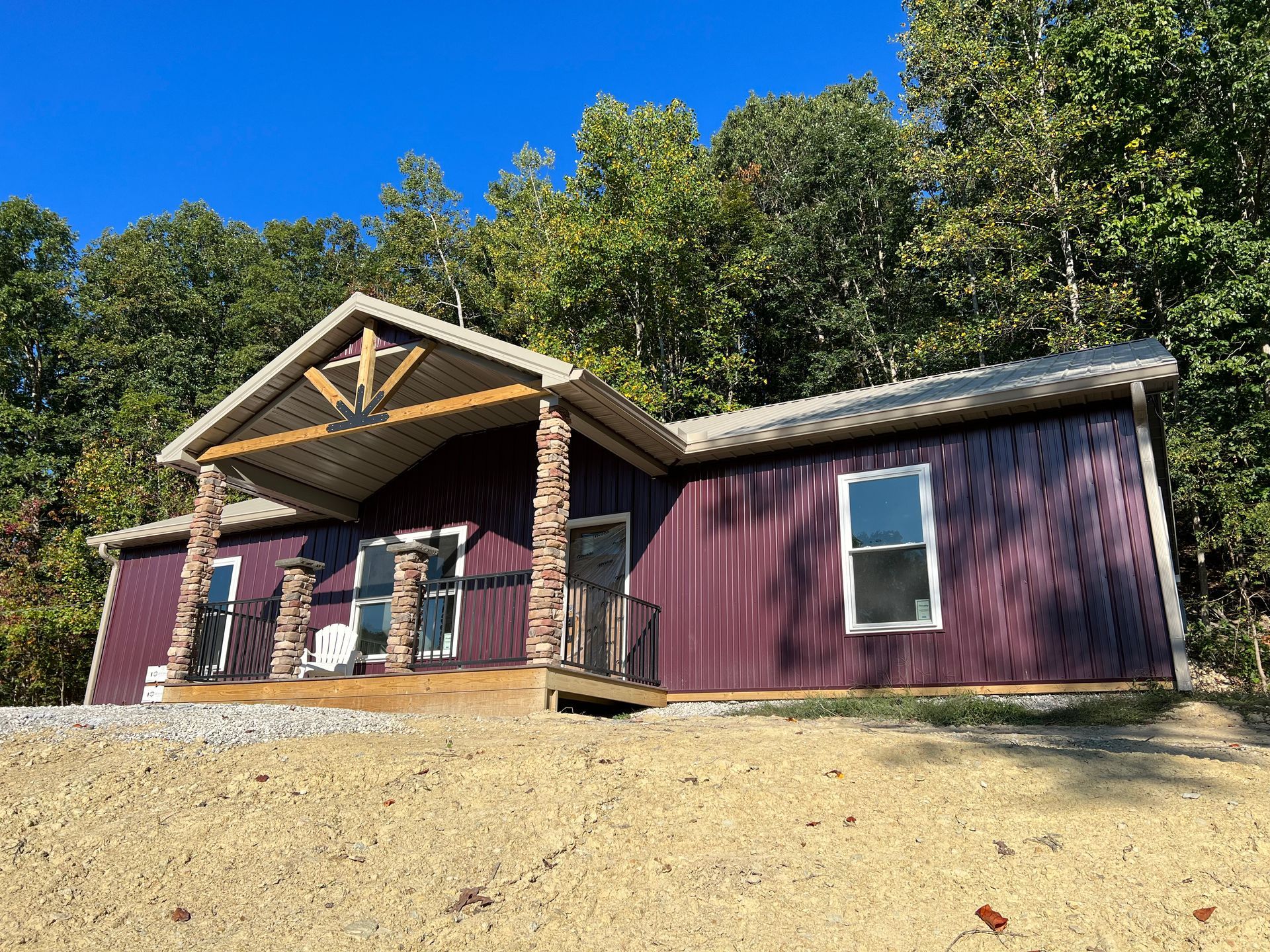 Purple cabin with a porch, nestled in a wooded area under a bright blue sky.
