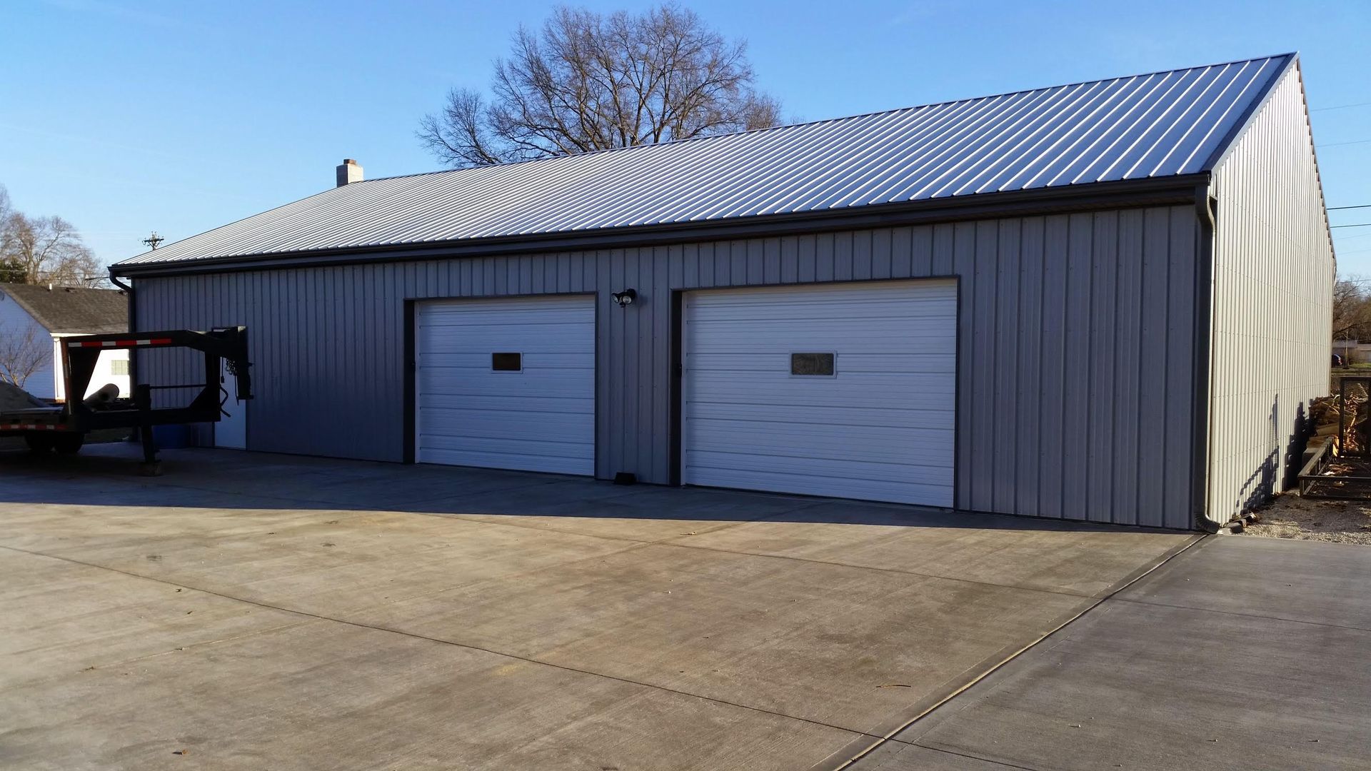 Two-bay metal garage with white garage doors and a corrugated silver roof. The garage is gray and sits on a concrete surface.