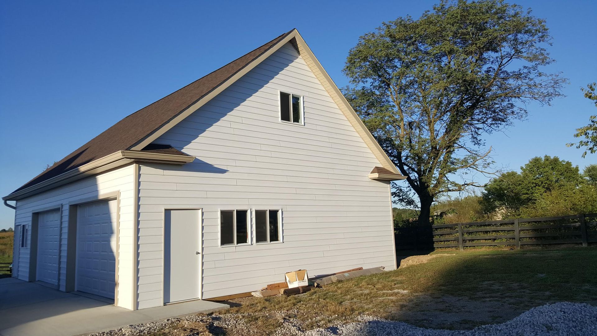 Two-story white building with garage doors and a pitched roof; a tree and fence are in the background.