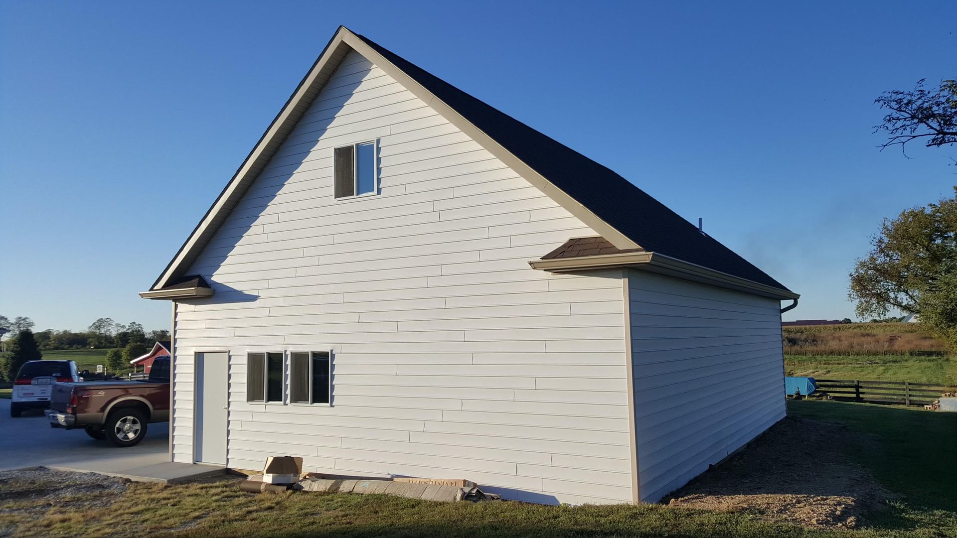White-sided two-story building with a dark roof, a small window, and a door. A brown truck is parked to the left.