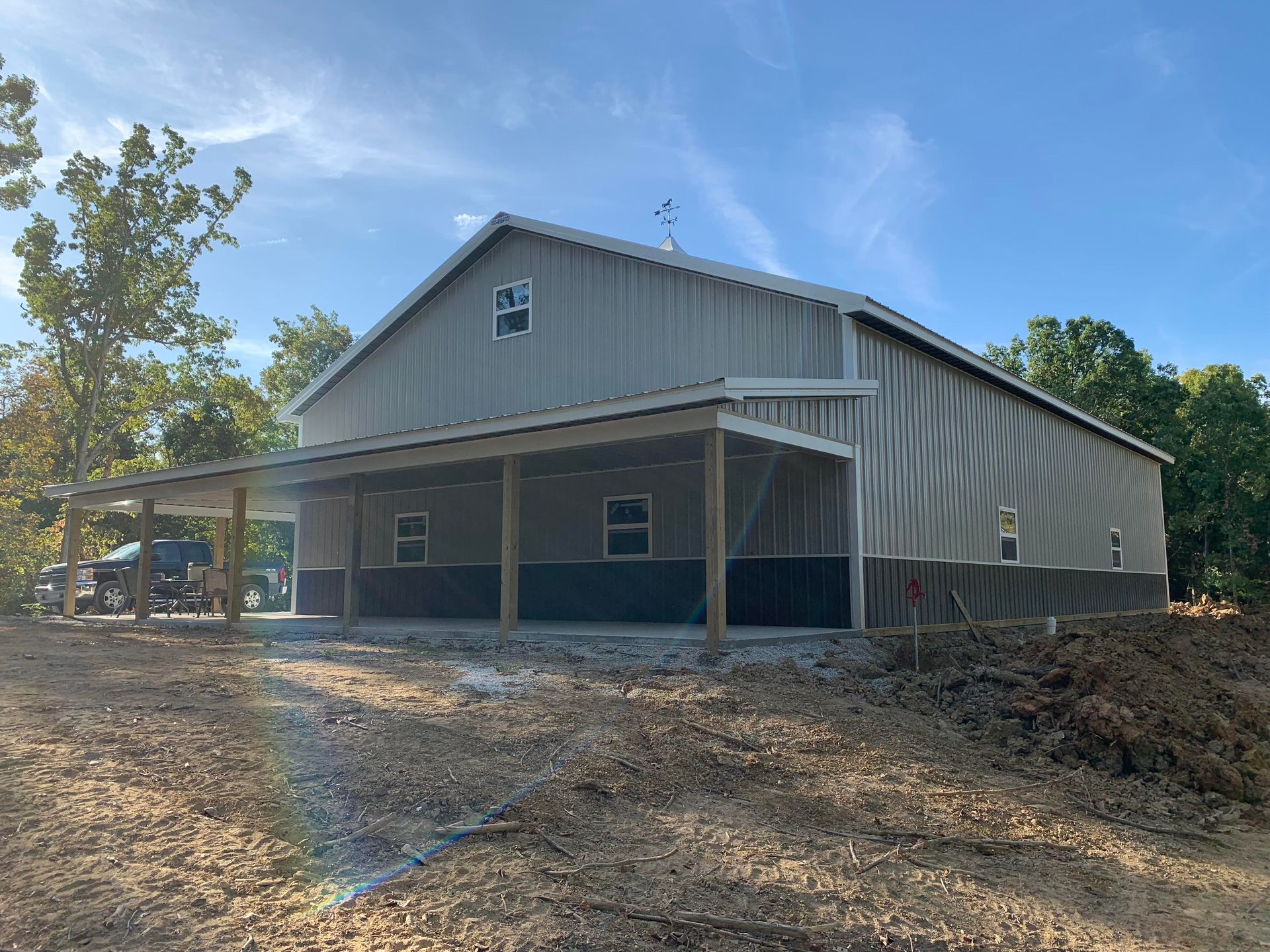 A large gray and black metal barn with a covered porch on a sunny day.