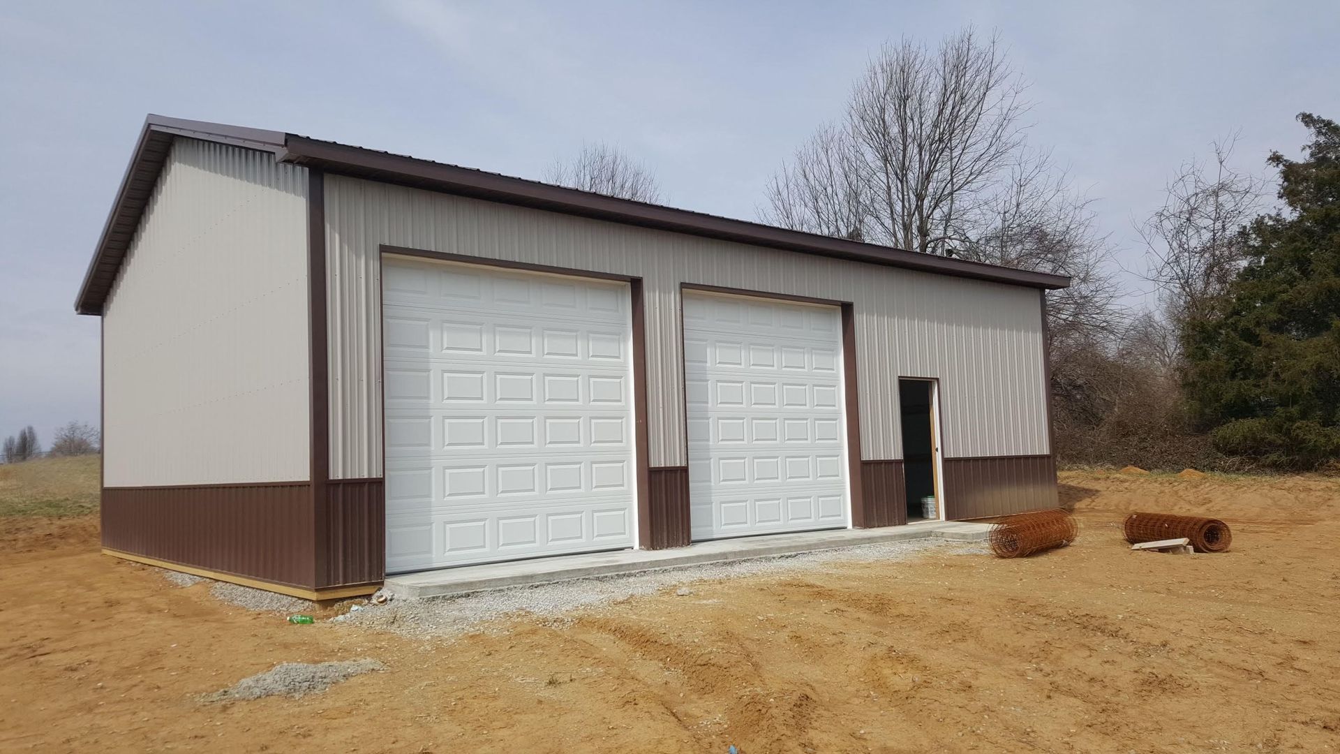 Two-car metal garage with brown trim and roof, white garage doors, set on a gravel base.