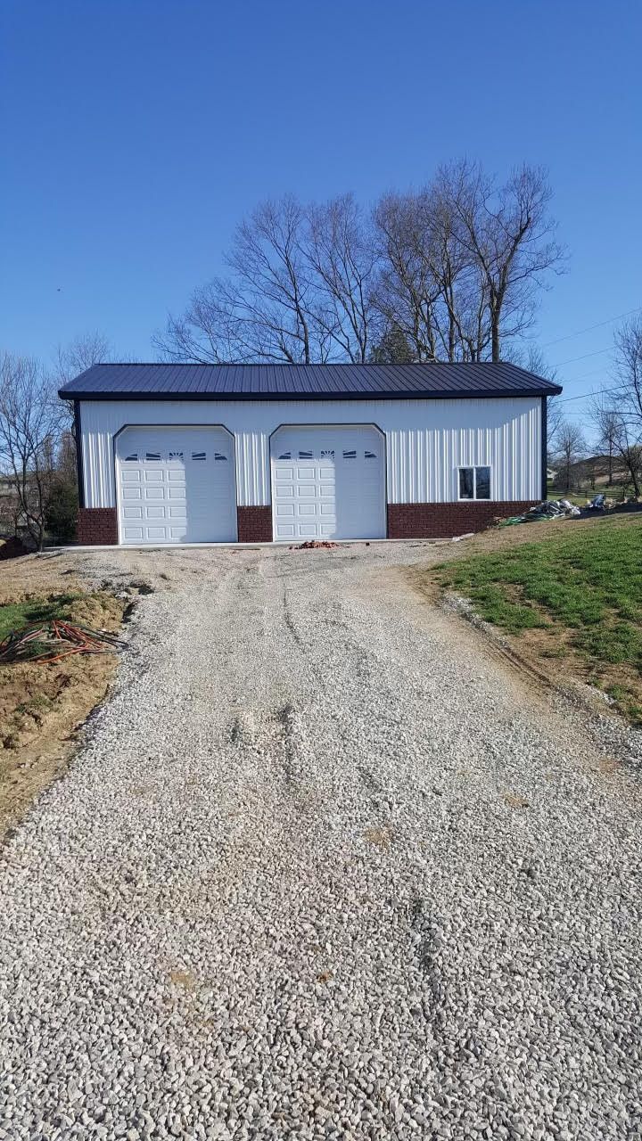 A white metal garage with two doors, a dark roof, and a gravel driveway under a blue sky.