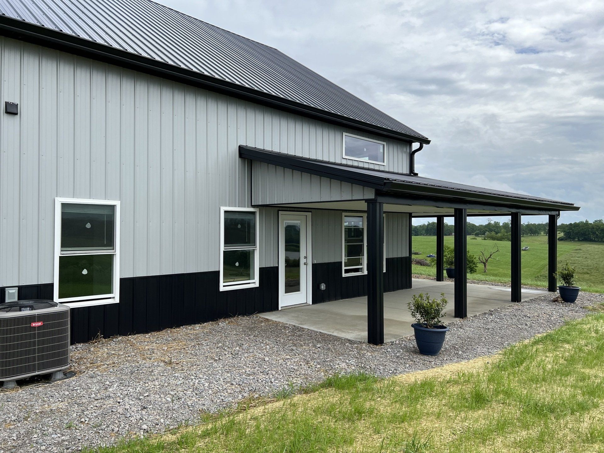 A modern gray and black building with a porch and metal roof. Gravel landscaping and a grassy yard are in the foreground.