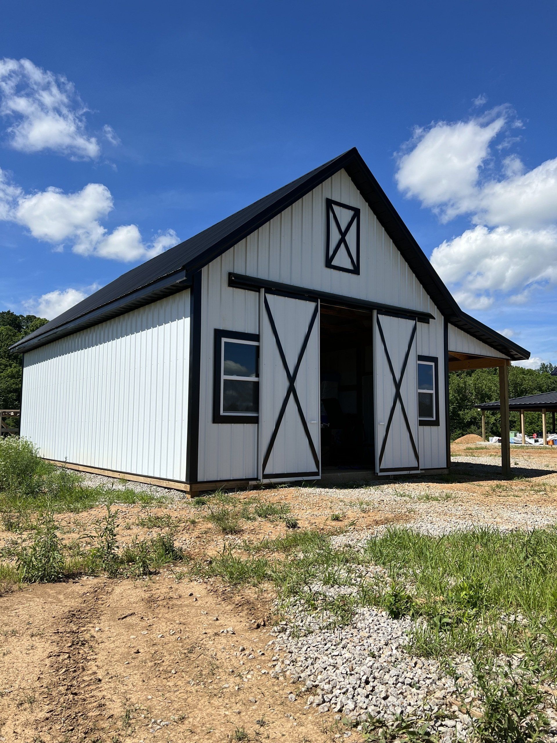 White barn with black trim and roof against a blue sky, with sliding barn doors and two small windows.