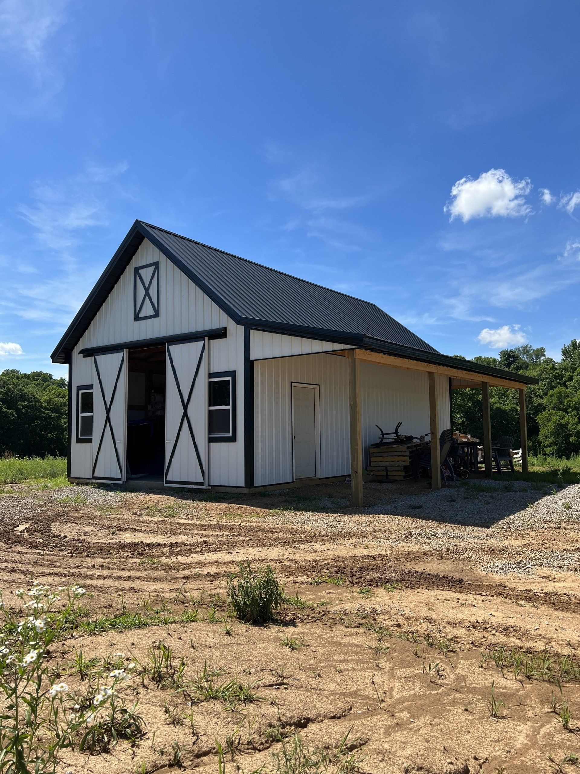White barn with black trim and roof, open doors, a small porch, and surrounding dirt field under a blue sky.