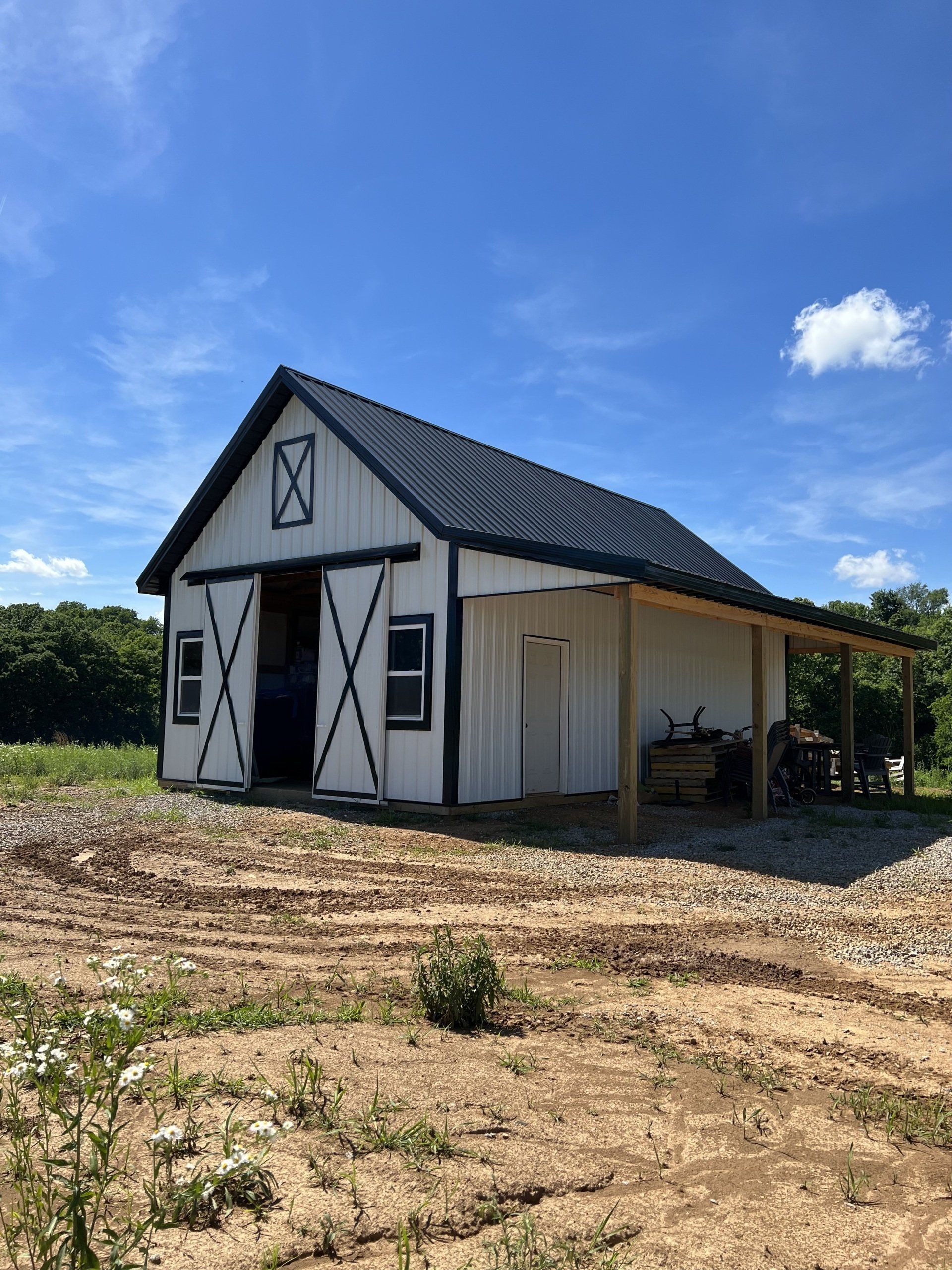 White and black barn with a black roof and porch under a blue sky. Set in a grassy field.
