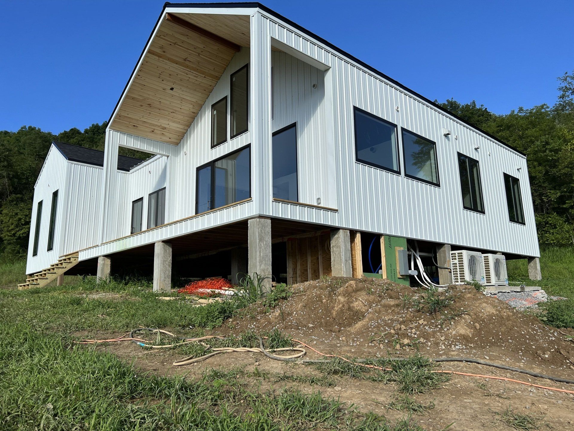 Modern white house under construction on a grassy hillside, featuring large windows and a wooden ceiling under the angled roof.