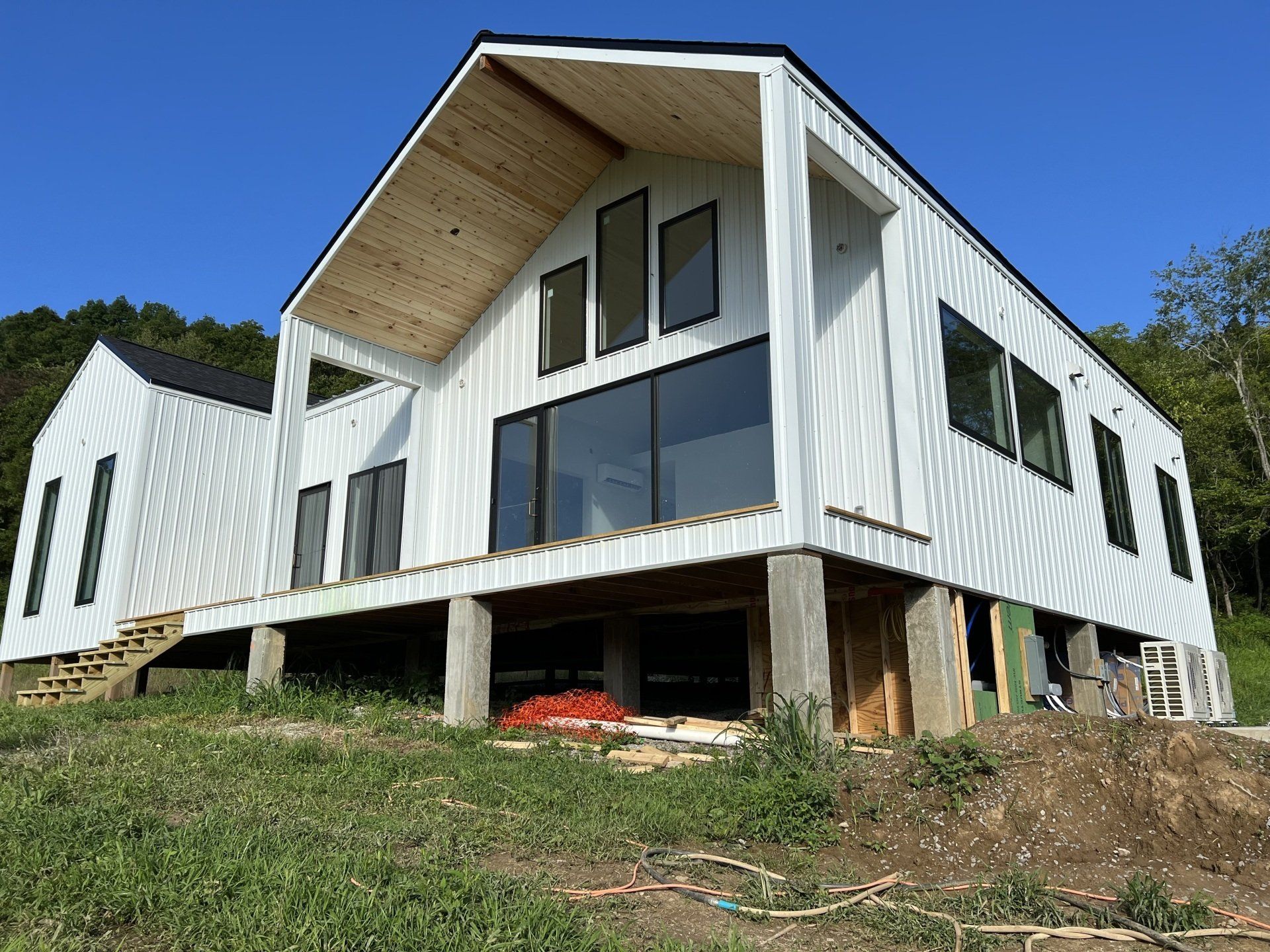 White modern house under construction with large windows, set on a grassy hillside against a blue sky.