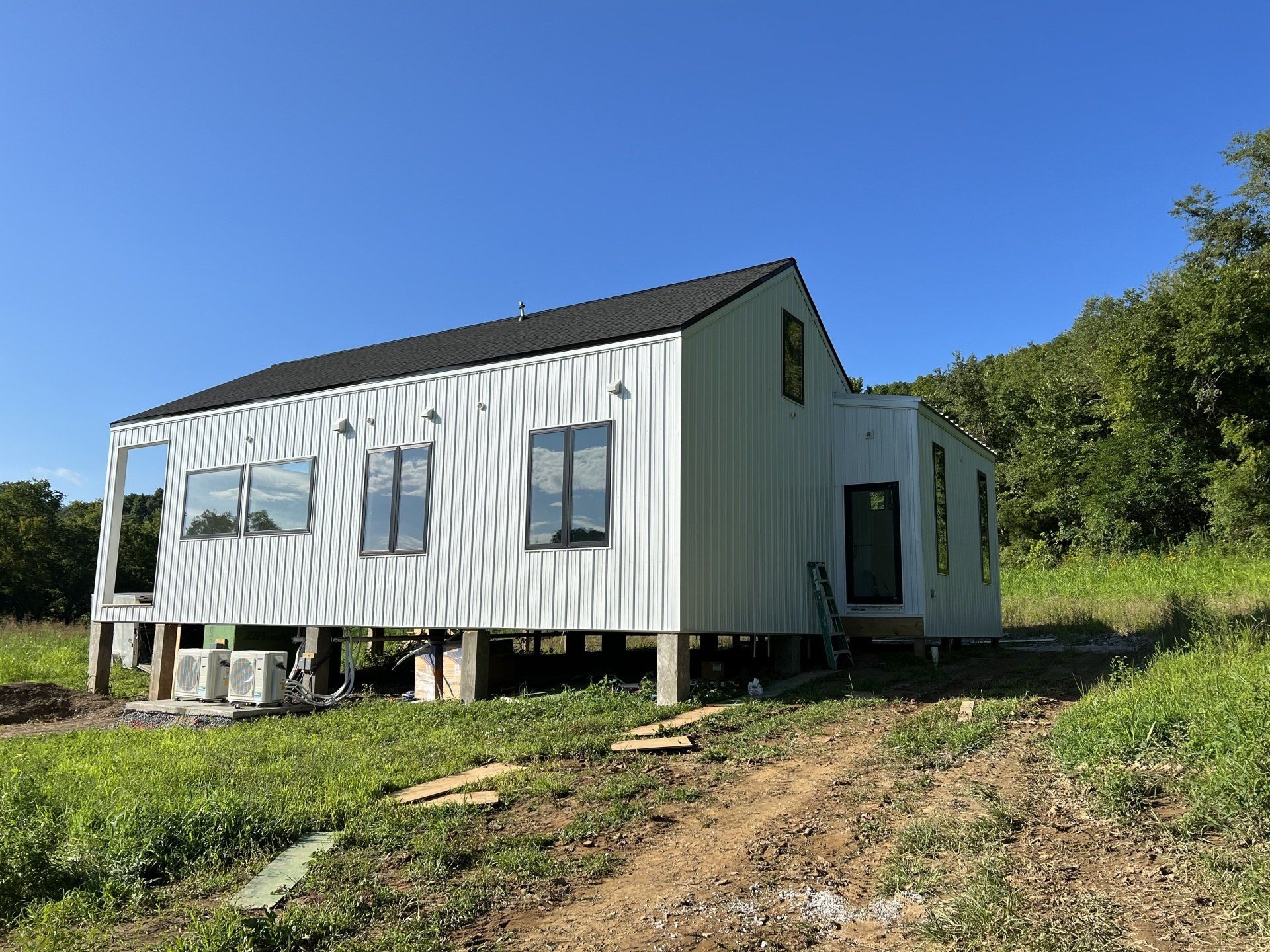 White house under construction on a grassy hill. Black windows and roof contrast with the white siding. A blue sky is overhead.