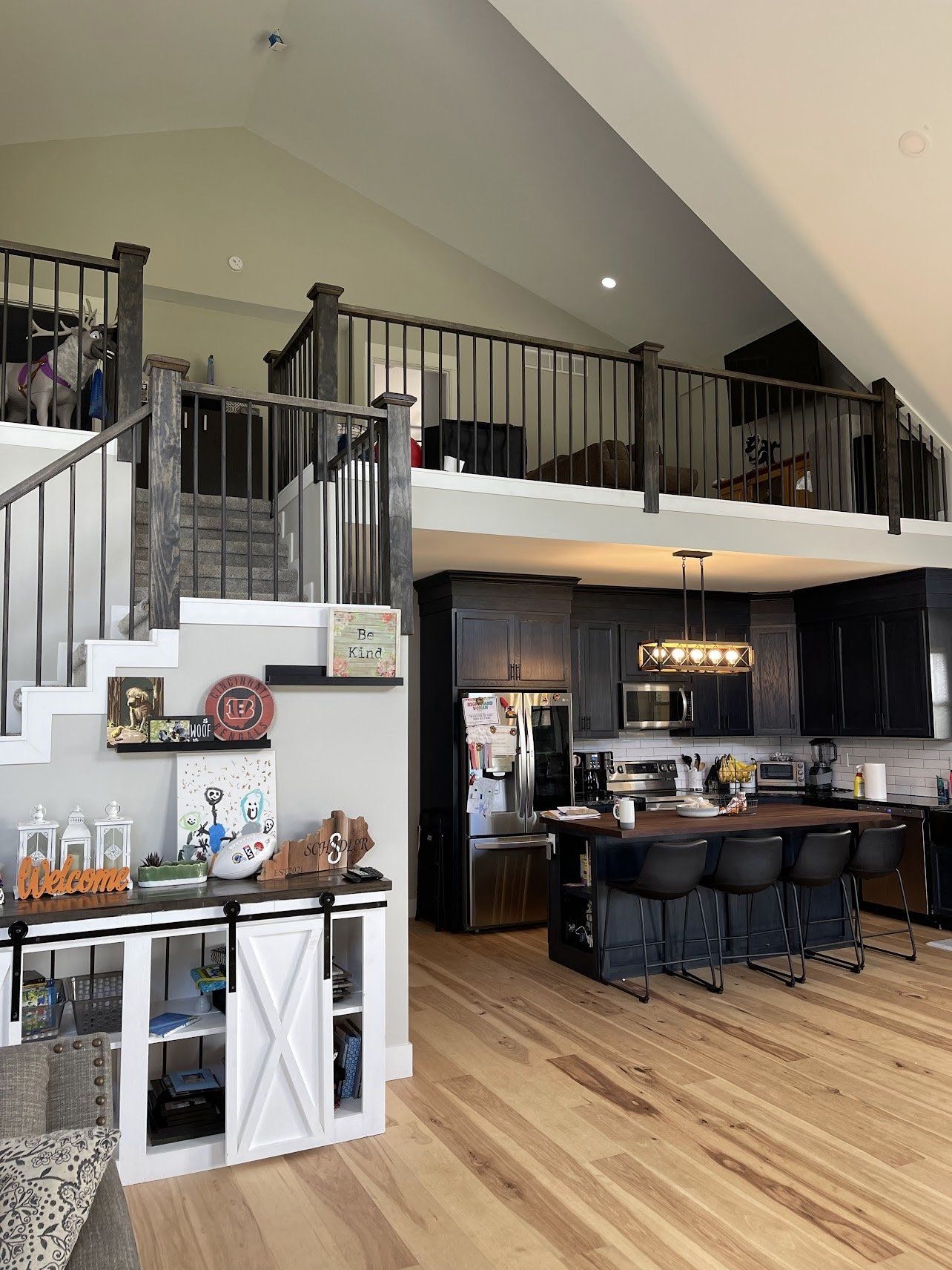 Interior view of a kitchen and loft area. Dark wood cabinets and island, light wood floors, and a staircase leading to a loft.