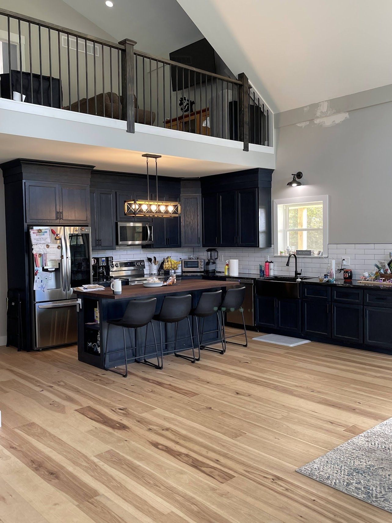 Kitchen with dark blue cabinets, a wooden island with seating, and a loft above. Light wood floors and gray walls.