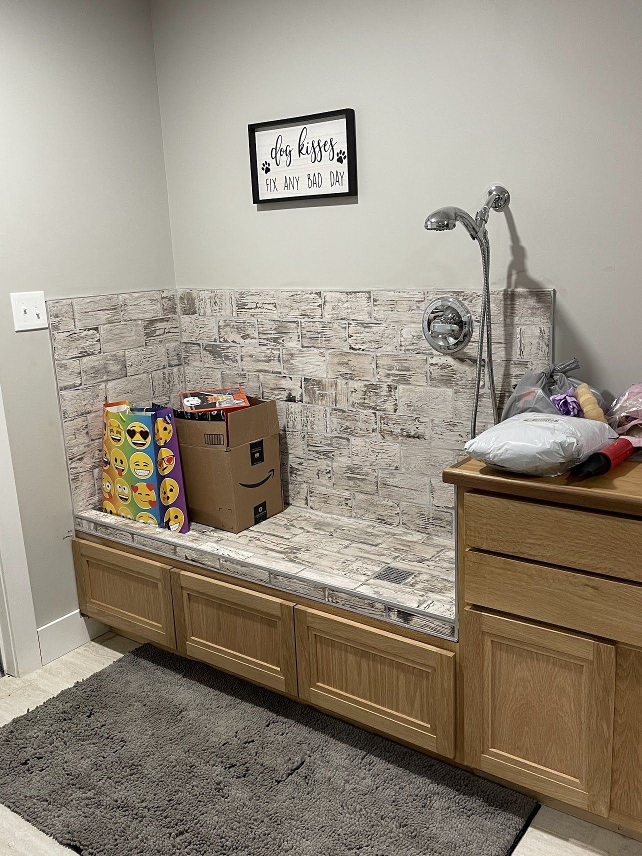 Dog washing station with a stone backsplash, cabinets, and a shower head. Gift bags and a box are on the countertop.