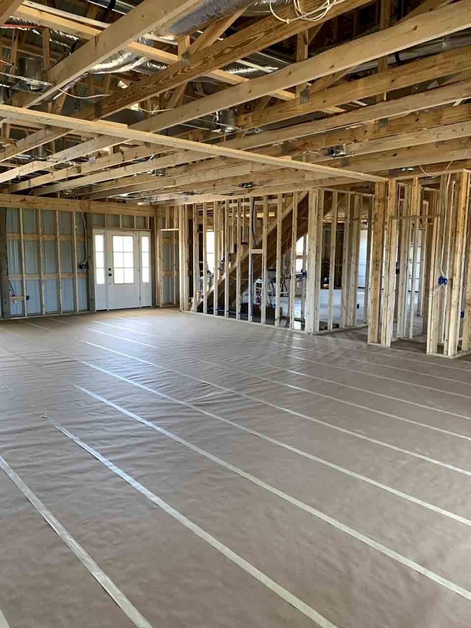 Interior view of a house under construction, showing wooden framing, exposed beams, and flooring covered with protective material.