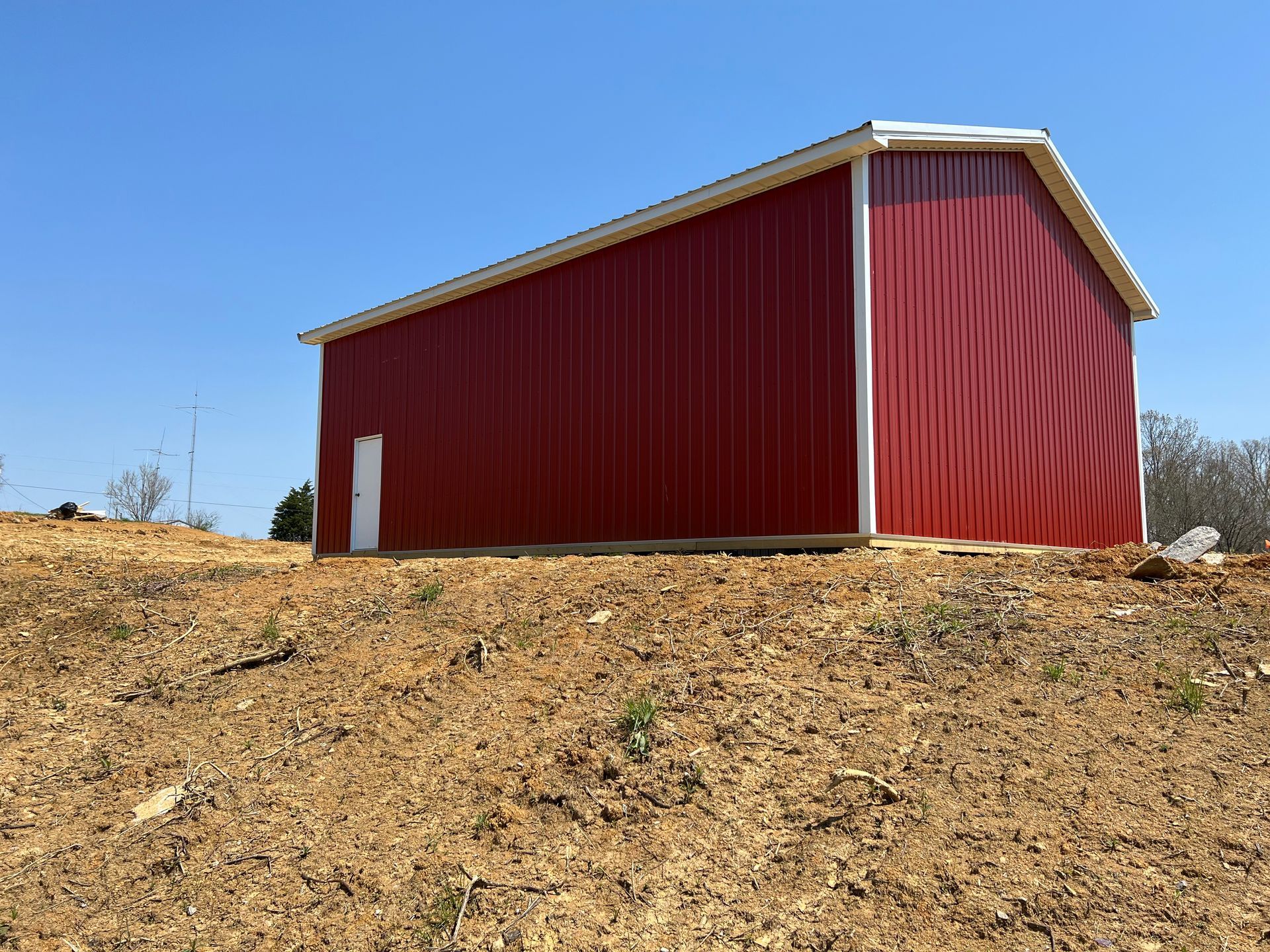Red barn with a white door and trim on a sunny, brown hillside.