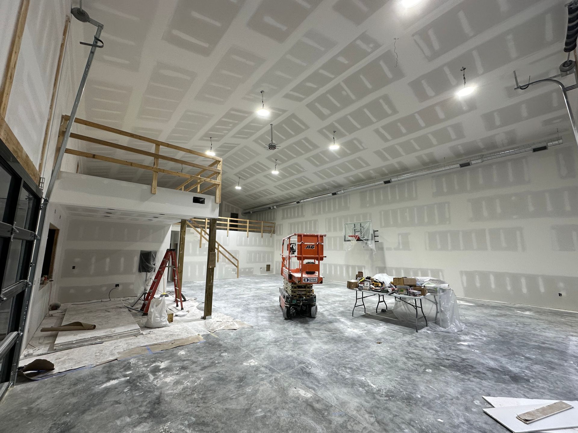 Interior of a large building under construction, with drywall installed on the walls and ceiling. An orange lift is in the center.