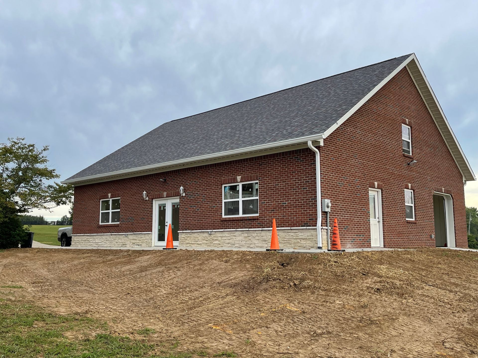 A brick building with a dark gray roof, white trim, and a light-colored brick base. Construction cones are in front.