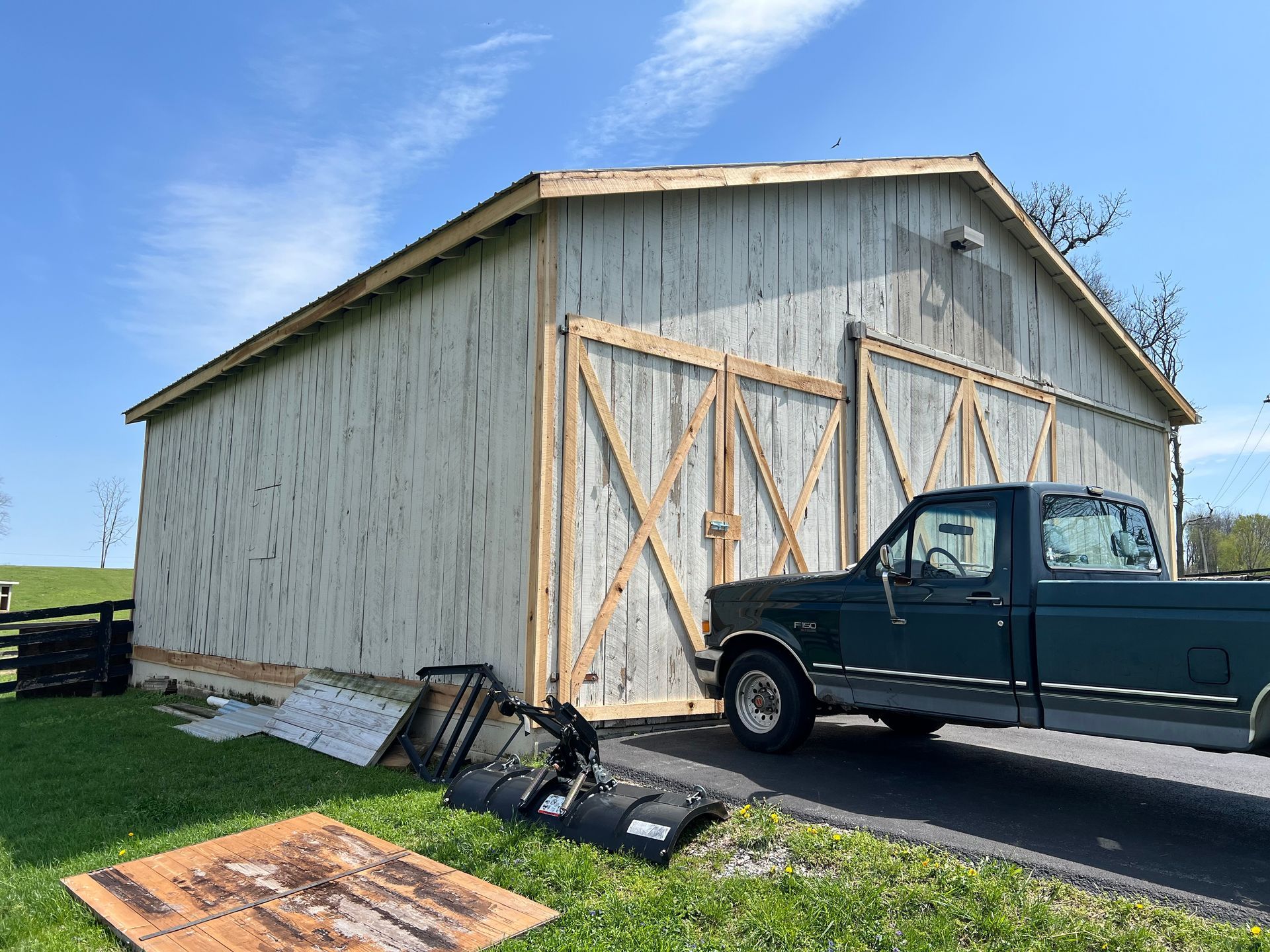 Barn with light-colored siding and wooden frame accents. A green pickup truck is parked on a paved driveway in front of the barn.