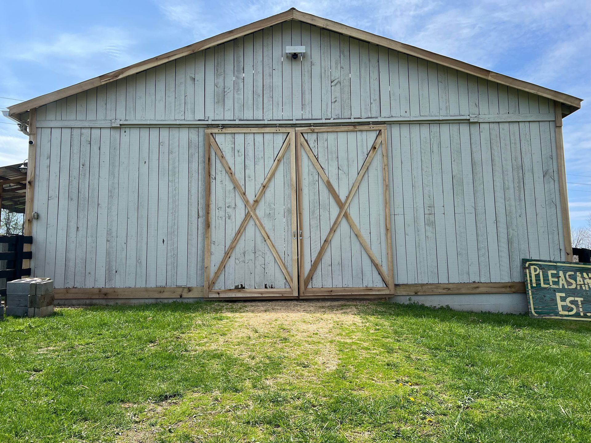 White barn with wooden doors and a green lawn. Sign on the right says, 